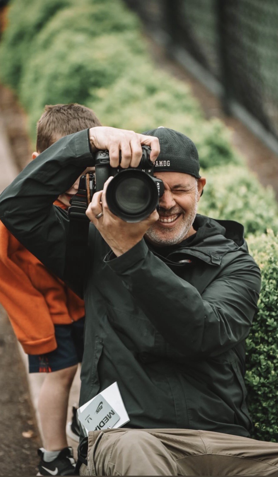 Chris Bates of Sideline Studio PDX, camera up and mid-laugh on the sideline