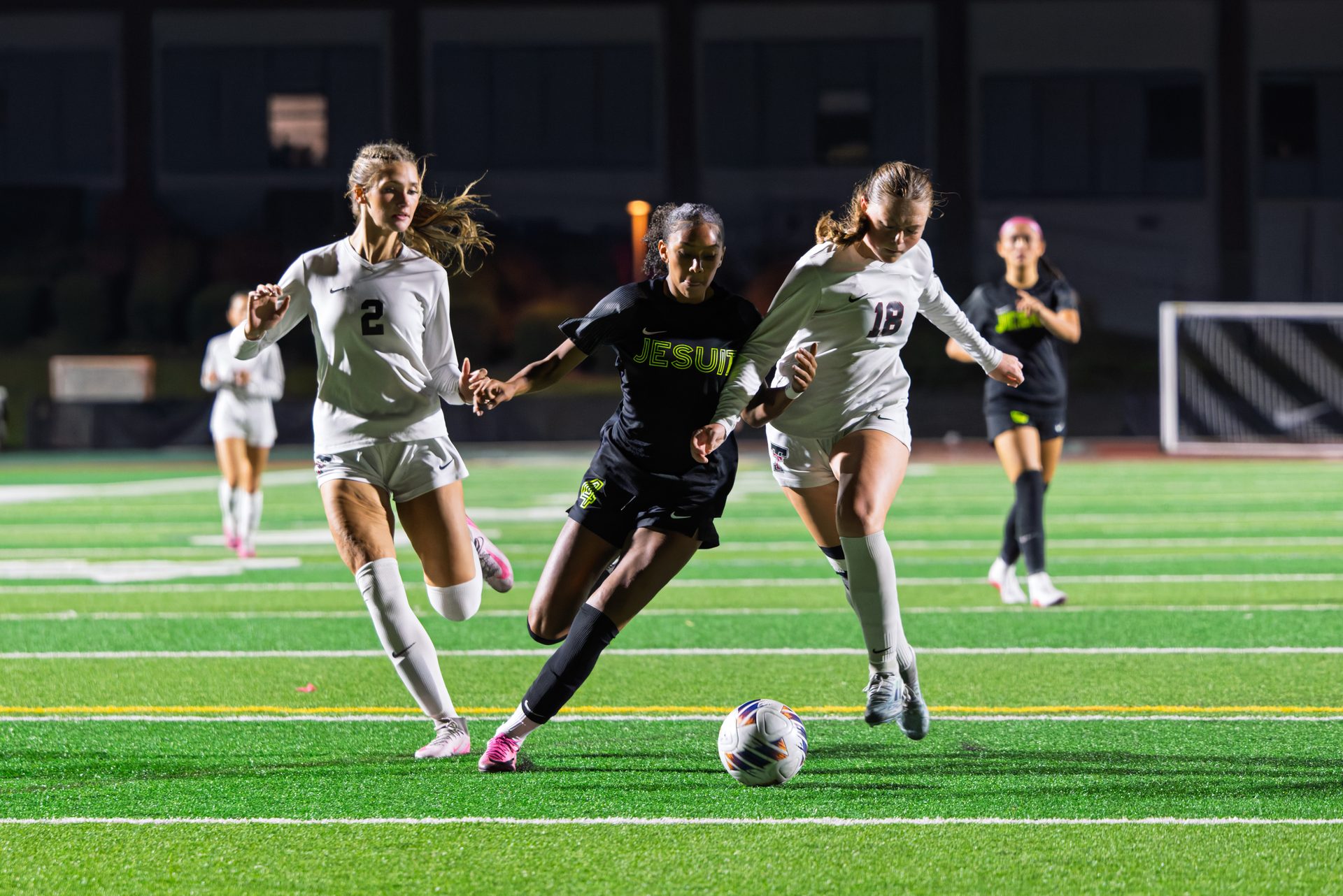 Under the bright lights, a player pushes the ball forward while two defenders close in from either side. Jesuit High School OSAA Soccer, Jesuit vs Tualatin, Jesuit HS, 2026.