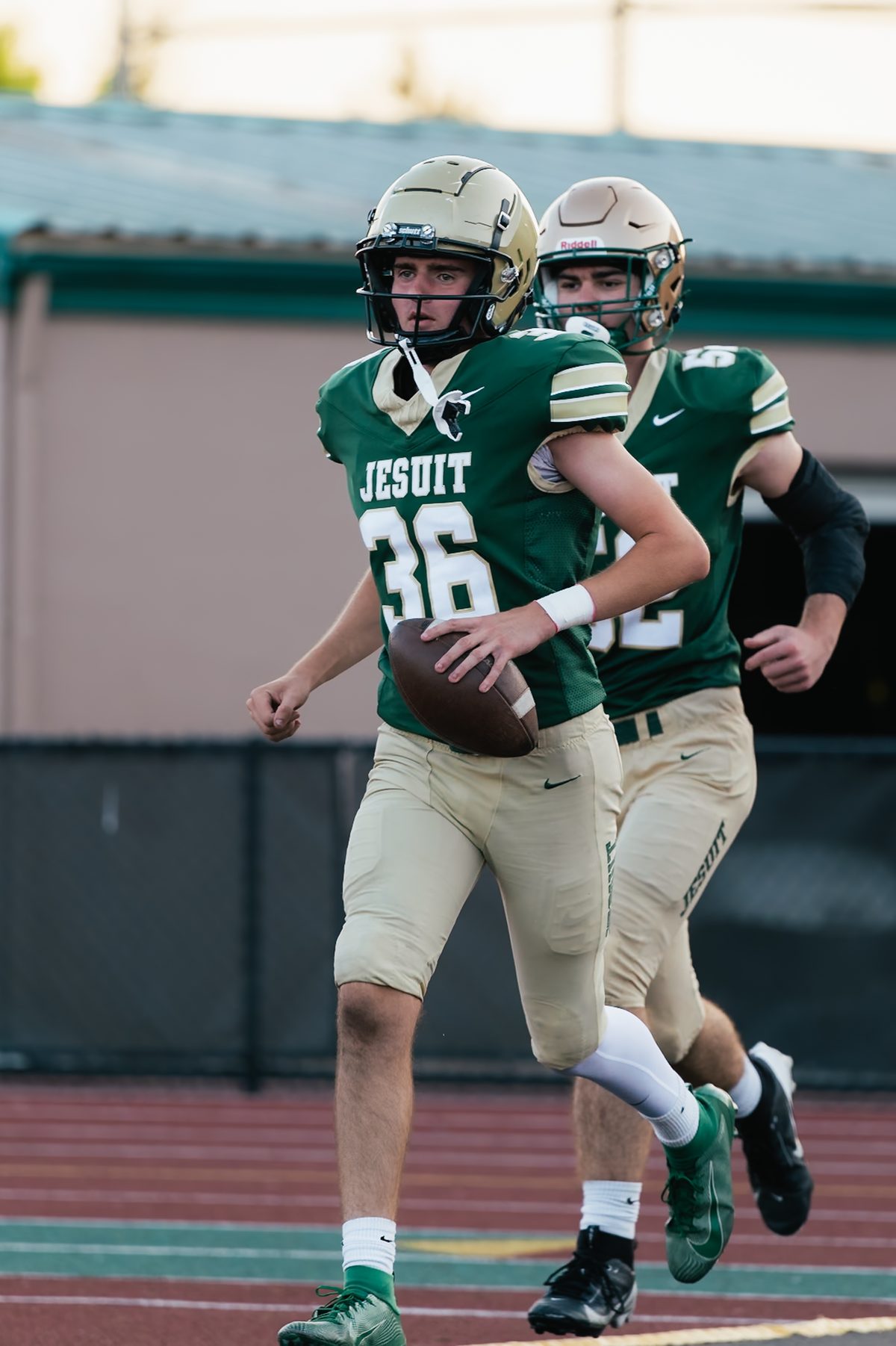 Jesuit football player jogging with the ball in uniform, directed action stills session.