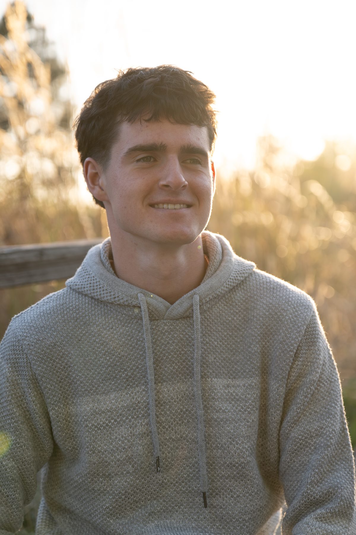Warm late-day light wraps around him as he smiles gently, looking off into the distance. Jesuit High School Senior Portrait, 2026.
