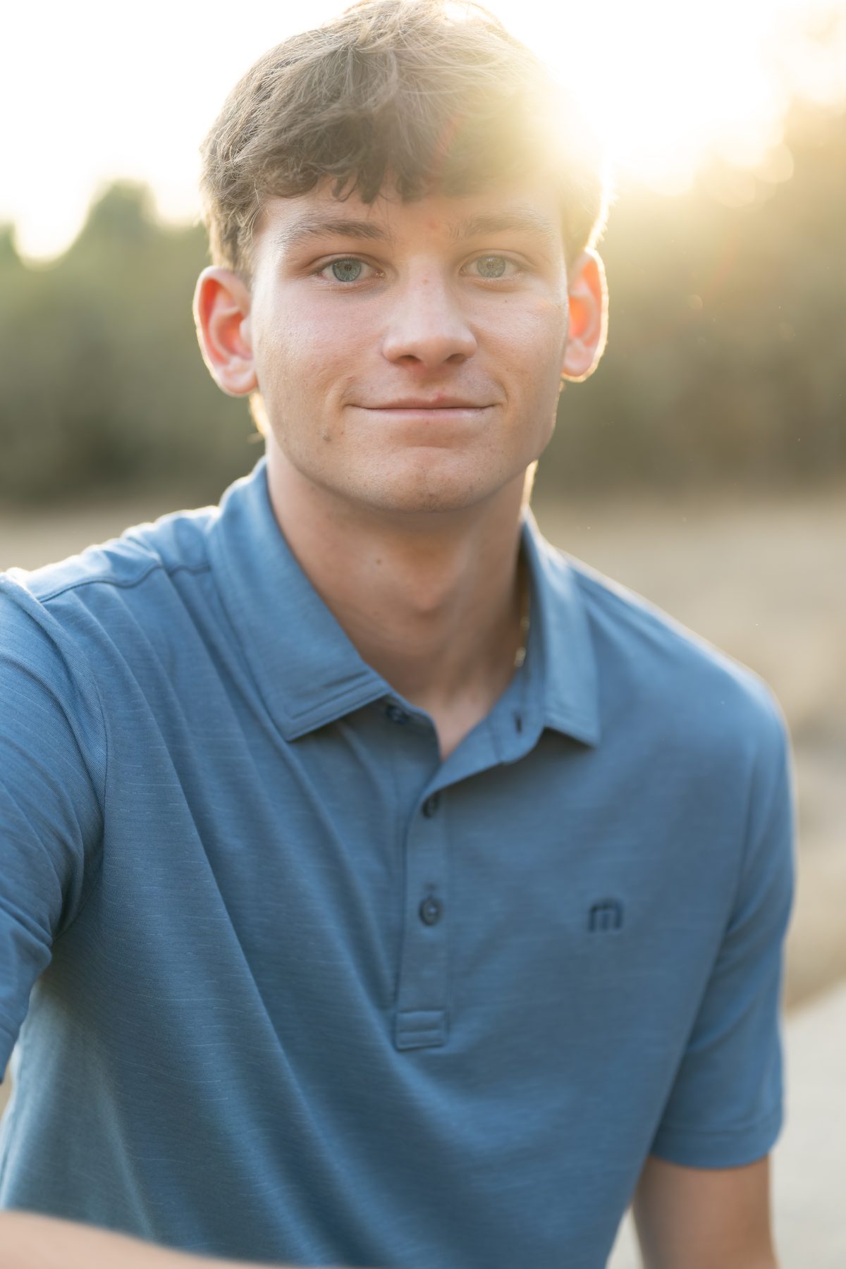 Warm late sunlight glows behind him as he offers a calm, easy smile for the camera. Jesuit High School Senior Portrait, 2026.