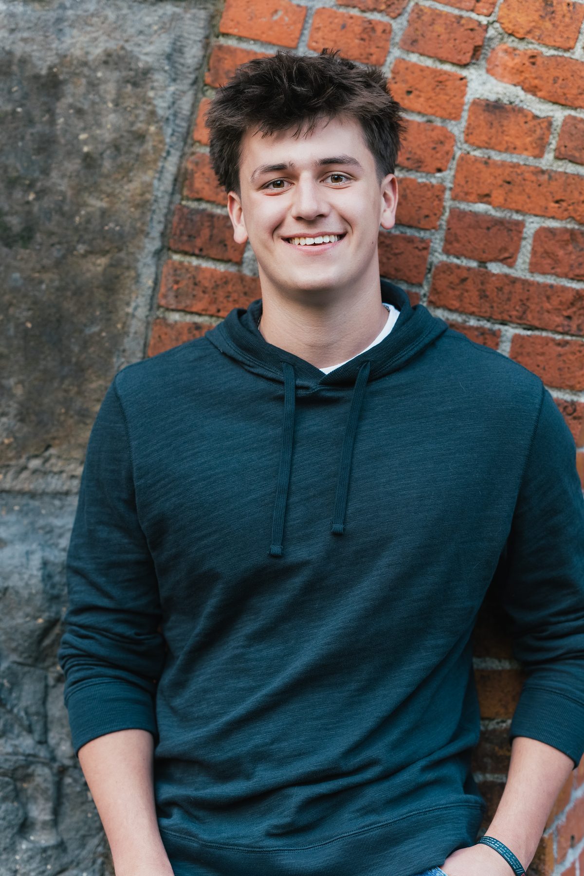 He leans against the brick wall with a relaxed smile, hands tucked into his pockets. Jesuit High School Senior Portrait, 2026.
