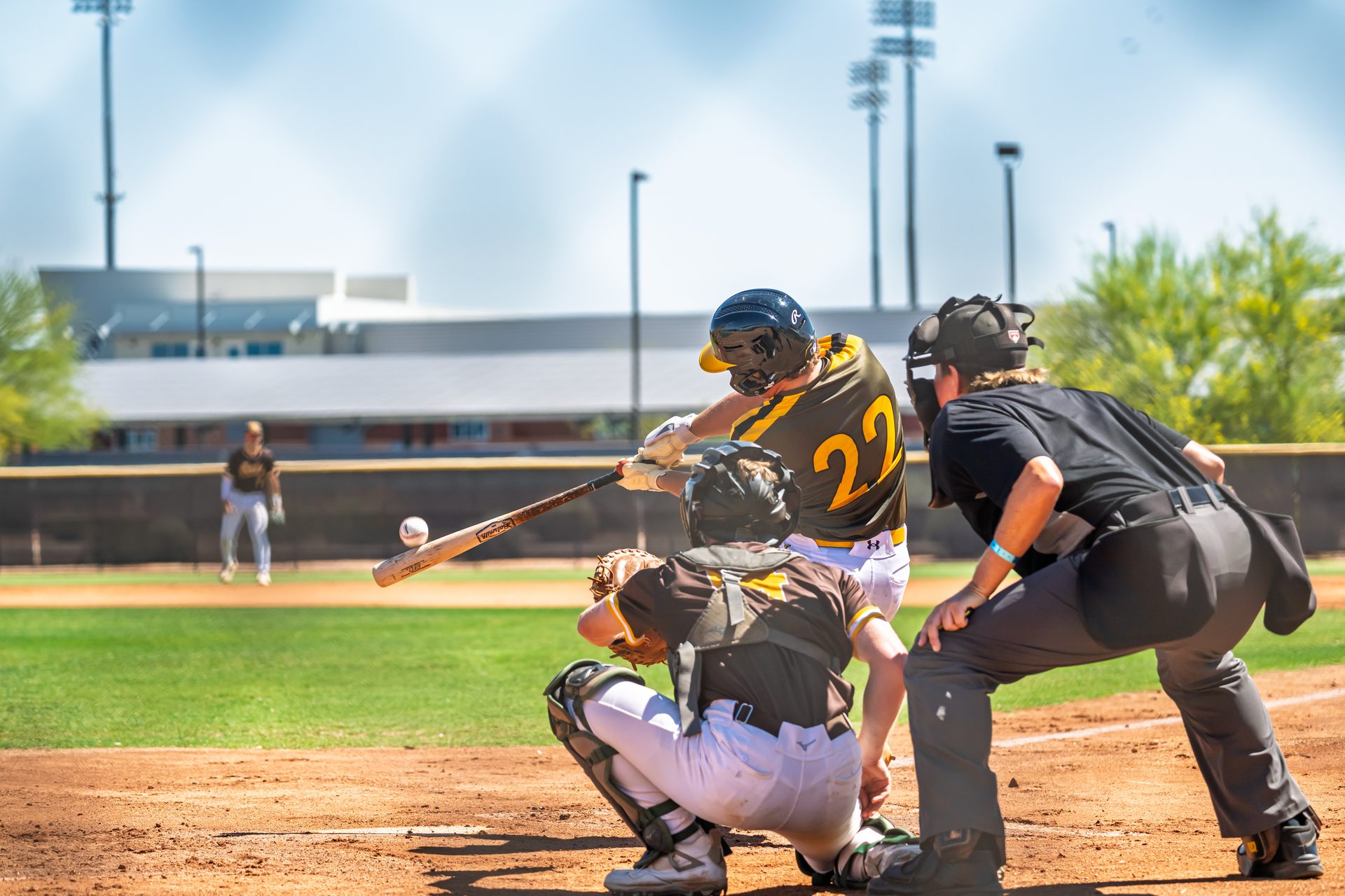 The crack of contact freezes the instant the ball leaves the bat while the catcher and umpire lean in for the call. Canes West 2027 Baseball, USA Baseball - AZ, 2026.