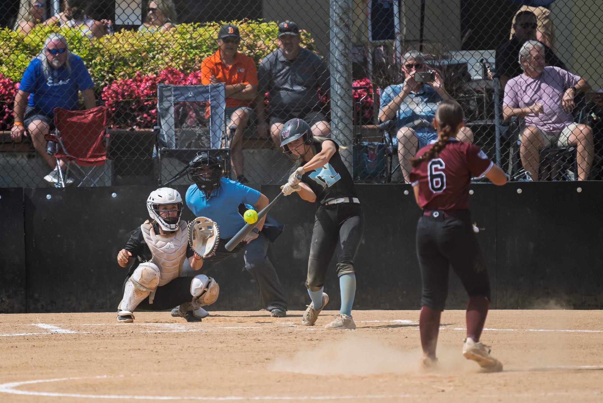 The batter drives through the pitch as the catcher and umpire watch closely behind the plate. 2026 TC World Series Softball, Opening Day, Portland, Oregon, 2026.
