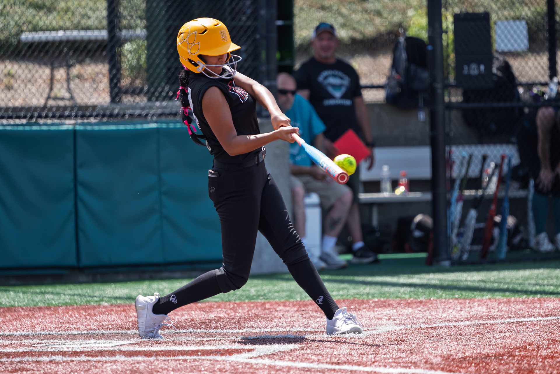 The batter's full swing meets the ball right at the plate, dirt scattering beneath her sneakers in the bright afternoon light. 2026 TC World Series Softball, Portland Oregon, 2026.