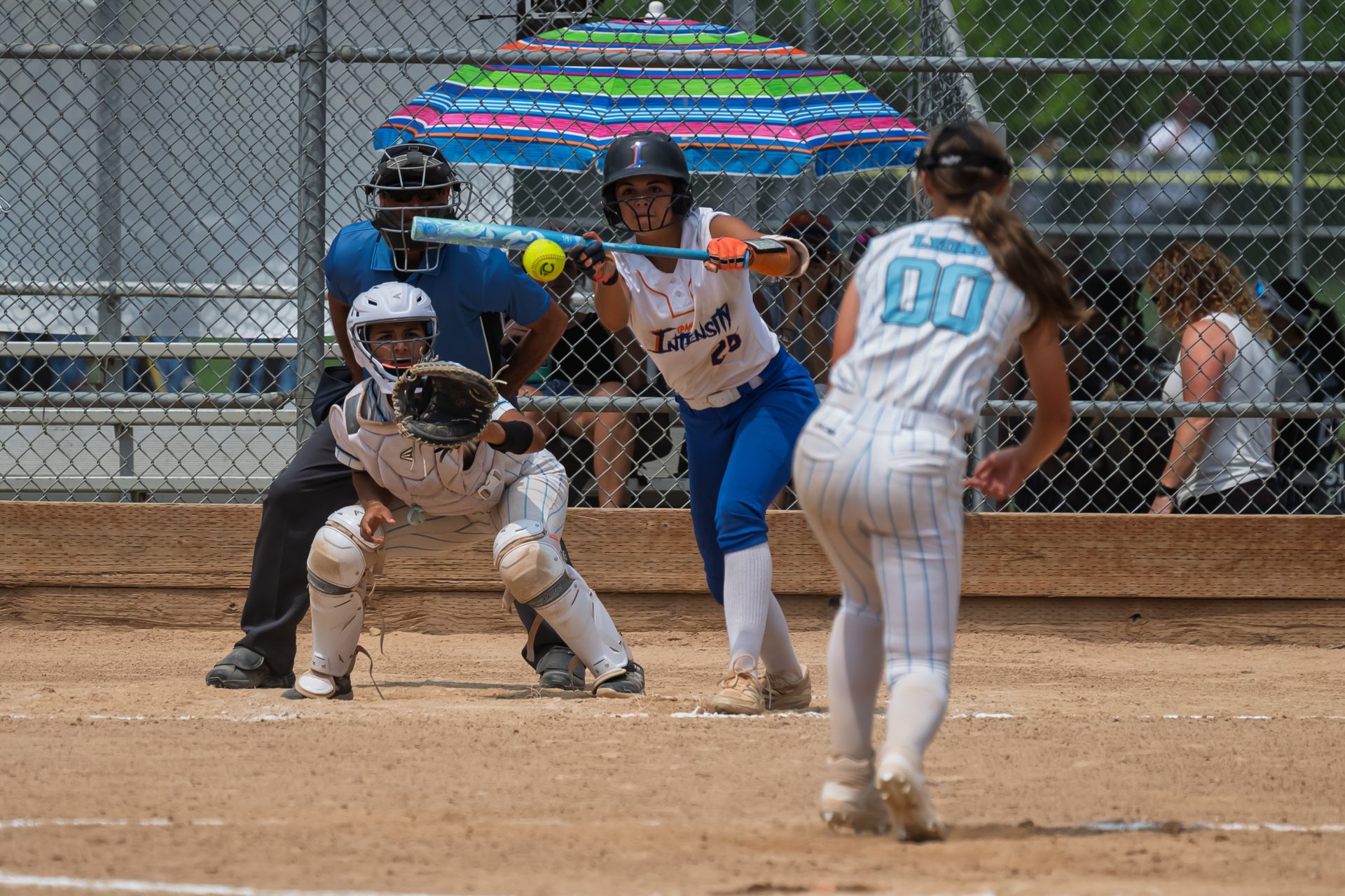 The batter times her swing as the yellow ball closes in, with the catcher and umpire crouched low behind the plate. 2026 TC World Series Softball, Portland Oregon, 2026.