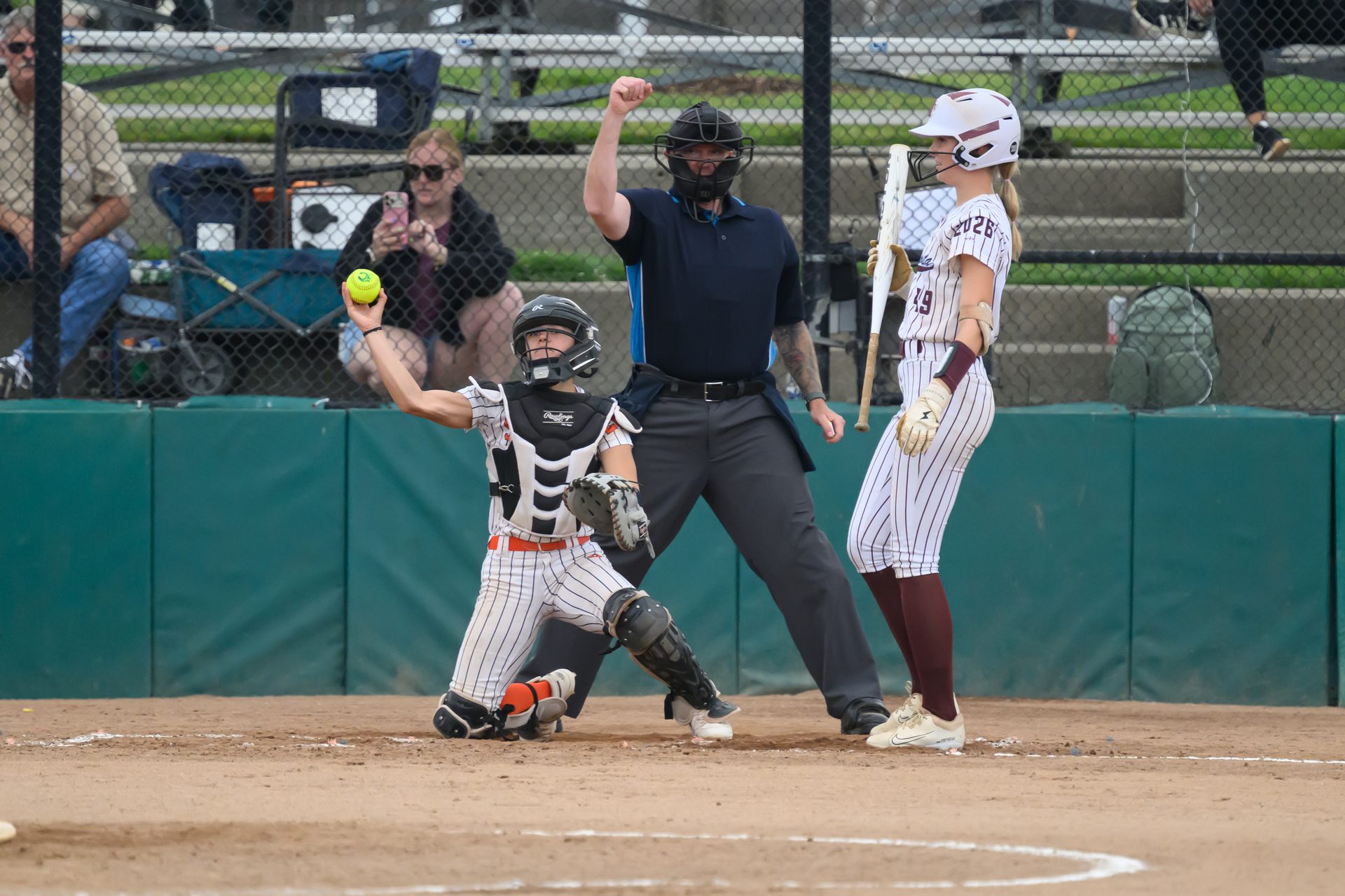 The catcher kneels and lifts the ball high as the umpire signals the call, while the batter waits with her bat ready. 2026 TC World Series Softball, Portland Oregon, 2026.