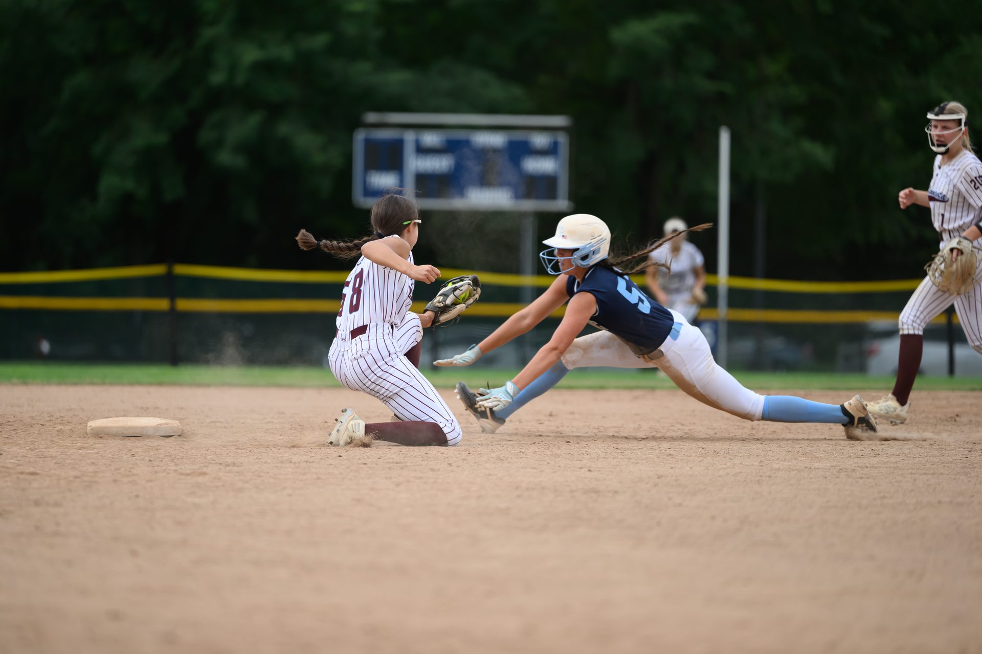 A runner dives low toward the base just as the fielder stretches out to make the catch. 2026 TC World Series Softball, Portland Oregon, 2026.