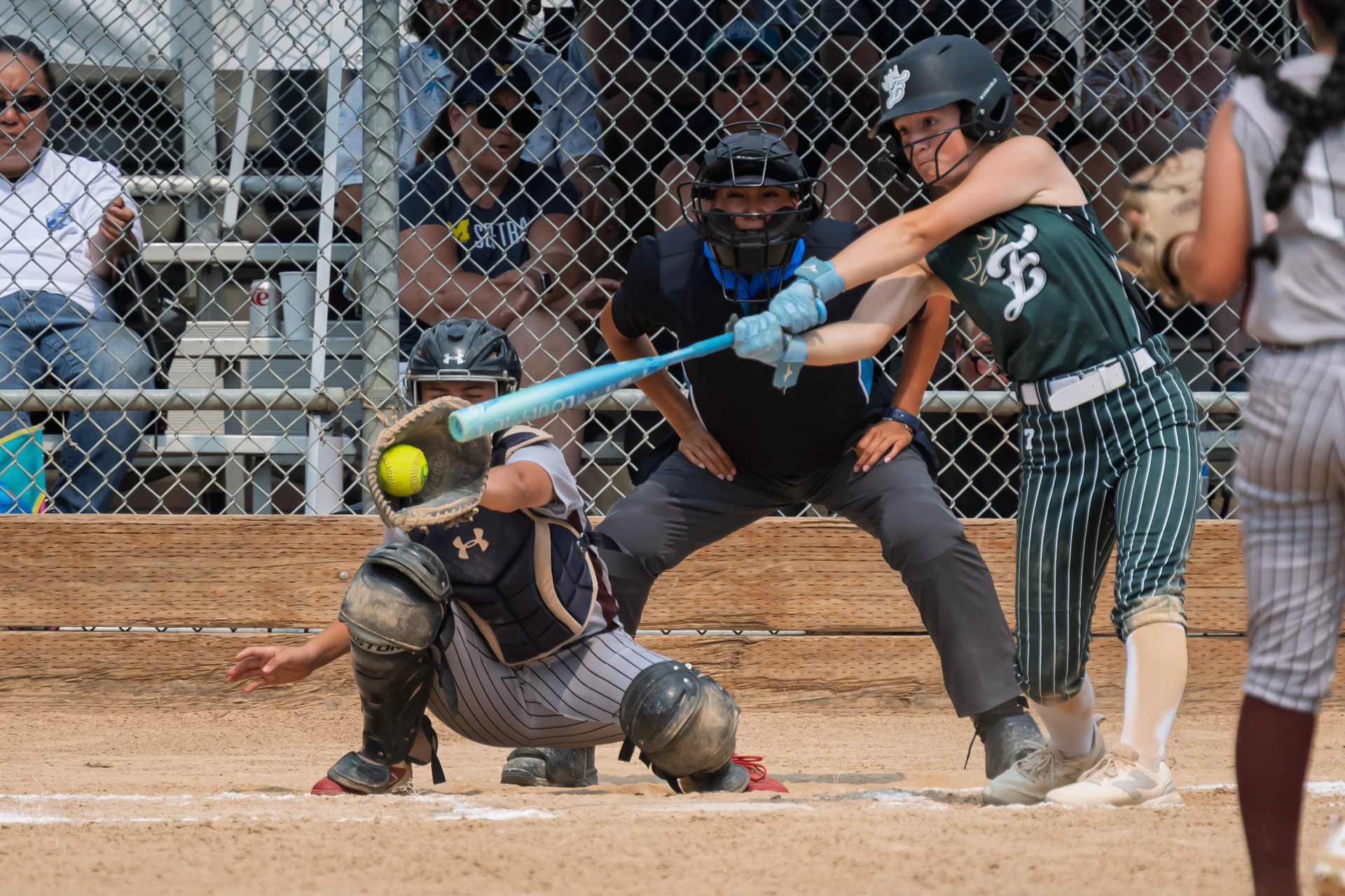 The batter times a swing as the catcher braces low behind the plate to receive the pitch. 2026 TC World Series Softball, Portland Oregon, 2026.