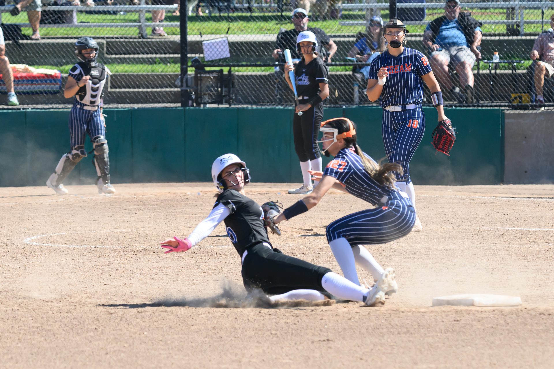 A runner kicks up a cloud of dust sliding into the base just as the defender reaches in for the tag. 2026 TC World Series Softball, Portland Oregon, 2026.
