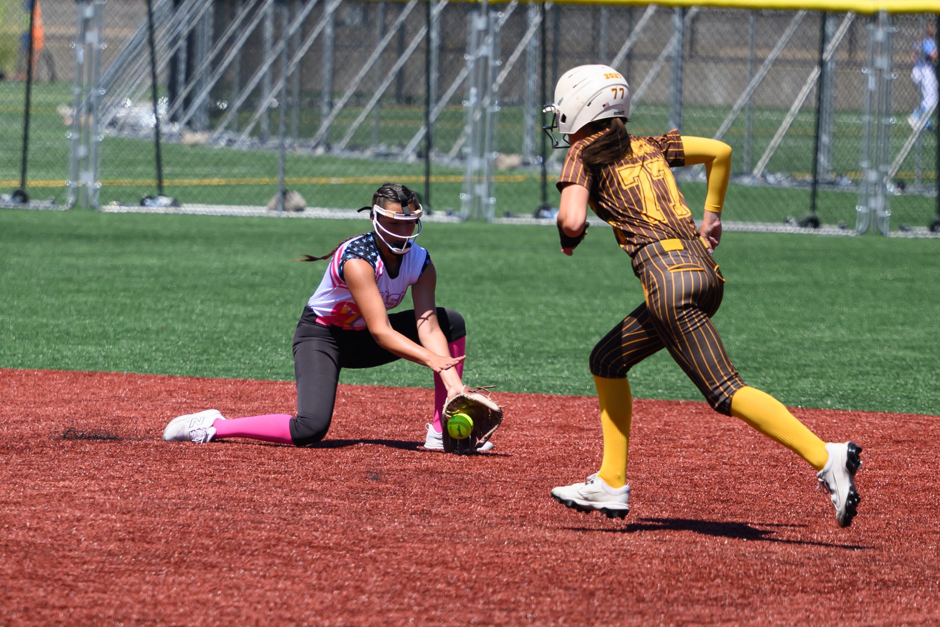 A kneeling infielder stretches to catch the ball just as the runner charges toward the base. 2026 TC World Series Softball, Portland Oregon, 2026.
