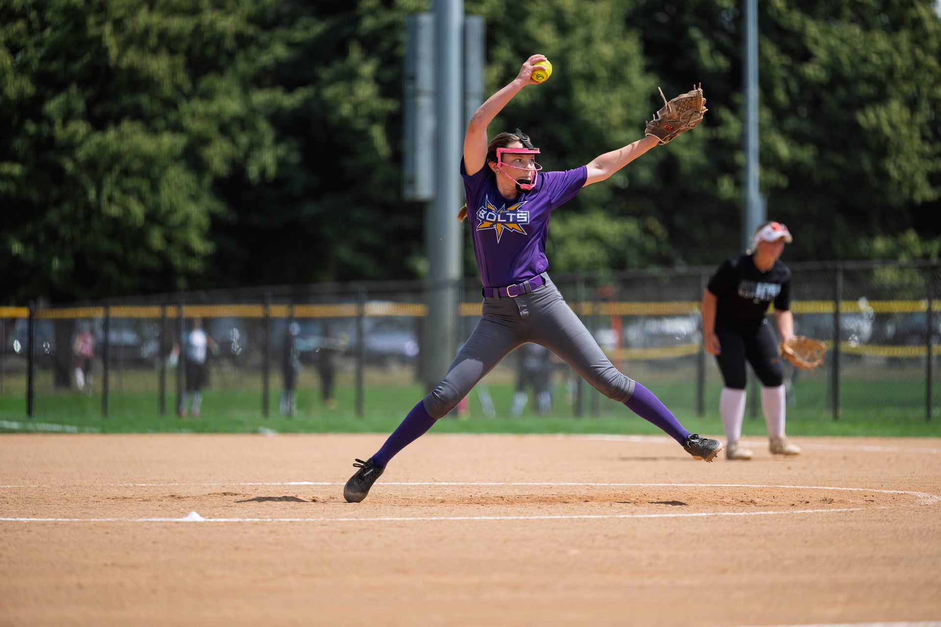 The pitcher stretches fully airborne, arm cocked back and legs split wide in the instant before the ball leaves her hand. 2026 TC World Series Softball, Opening Day, Portland, Oregon, 2026.