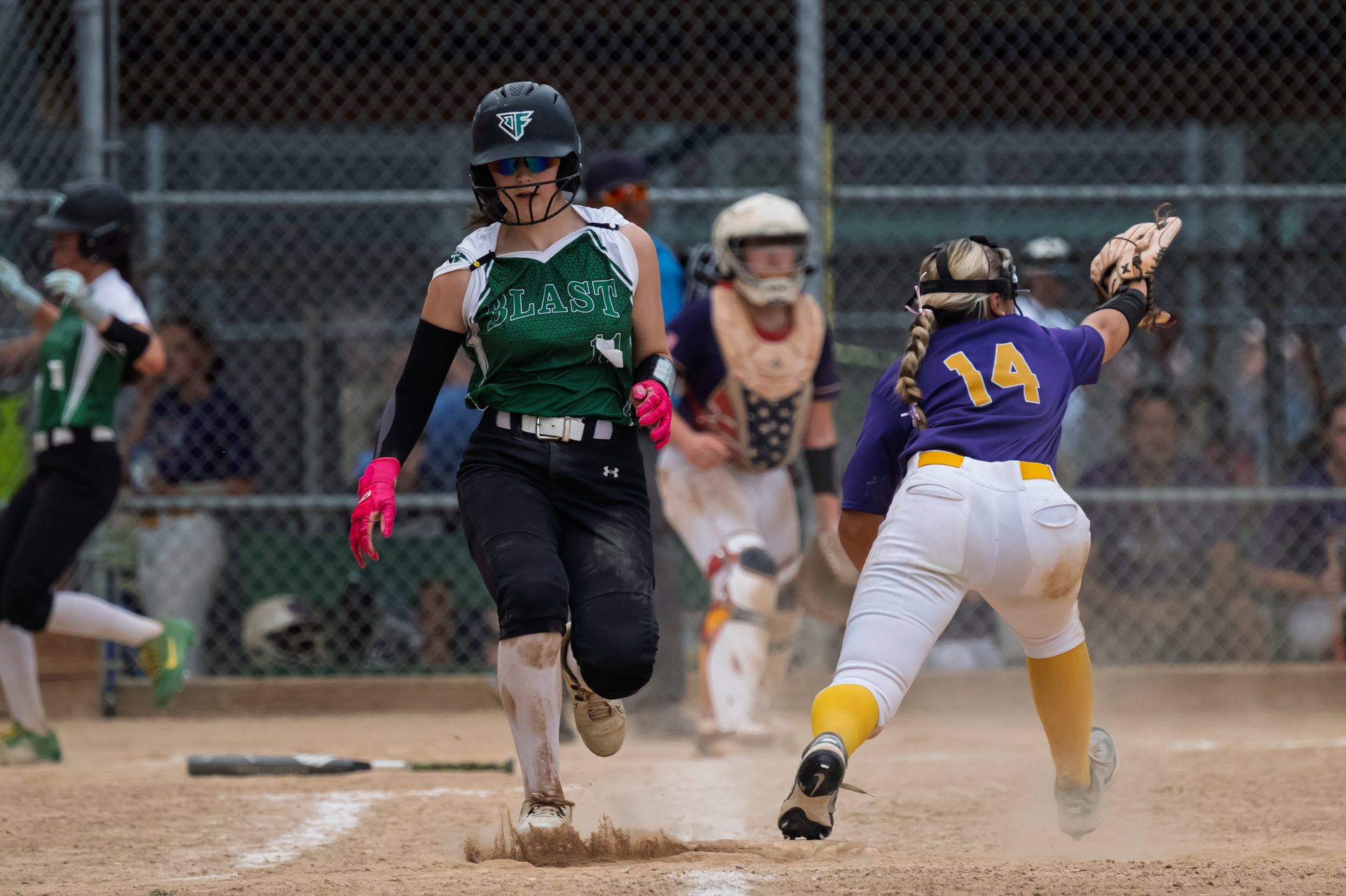 A runner kicks up dust racing toward home plate while a fielder stretches out for the throw. 2026 TC World Series Softball, Portland Oregon, 2026.